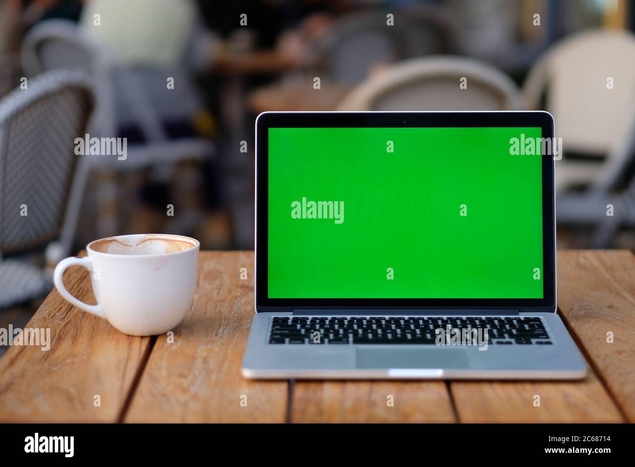 Nahaufnahme eines grünen Bildschirm Laptop-Computer auf Holztisch mit einer Tasse Kaffee. Blur Bürgersteig Café Hintergrund Stockfoto