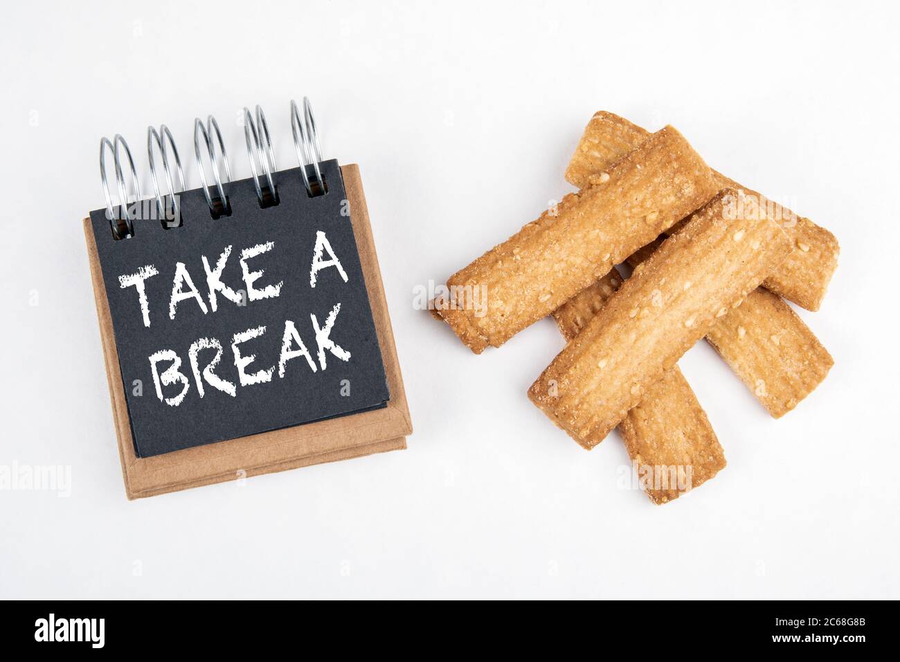 MACHEN SIE EINE PAUSE. Arbeit und Studium Last, Stress und Ruhe Konzept. Schwarzes Notizbuch und Cookies auf weißem Hintergrund Stockfoto