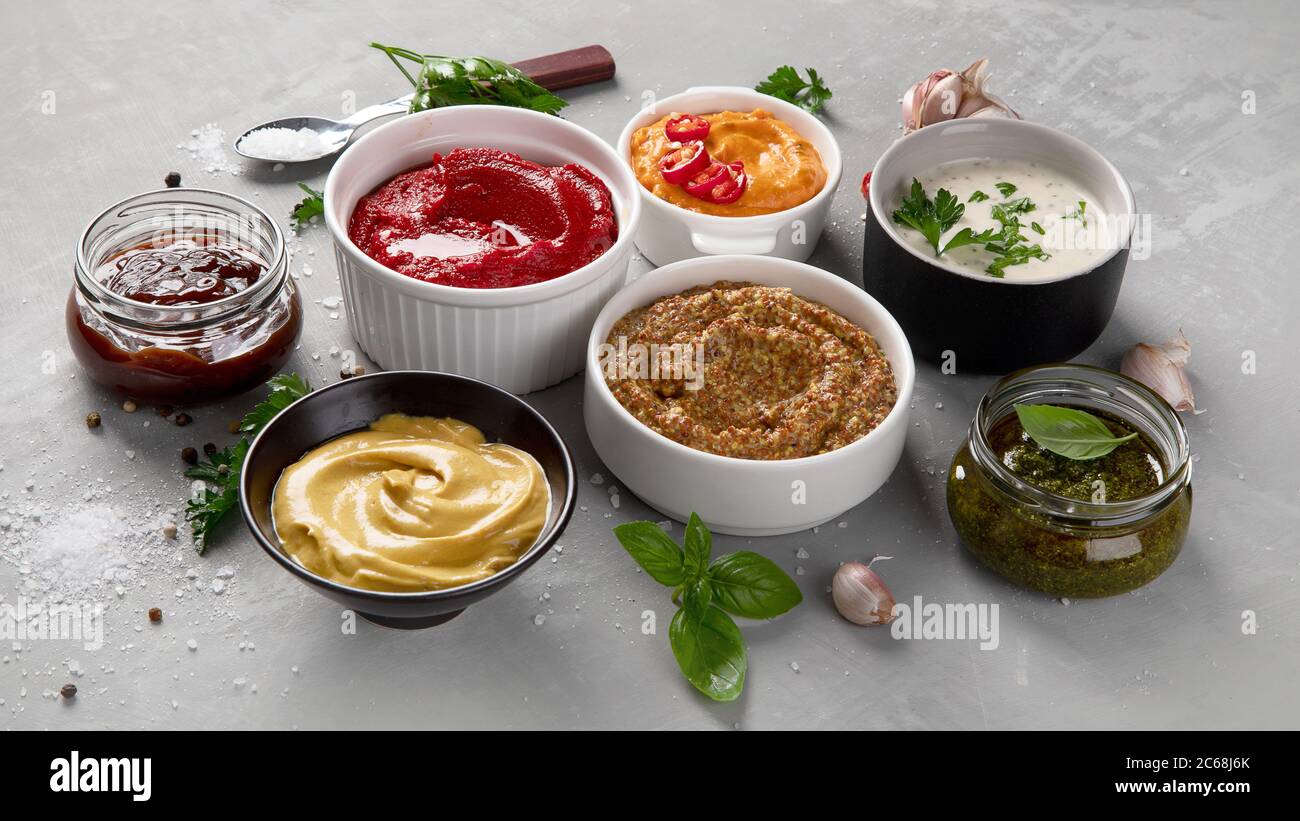 Set aus verschiedenen Saucen in Schalen auf grauem Hintergrund. Stockfoto