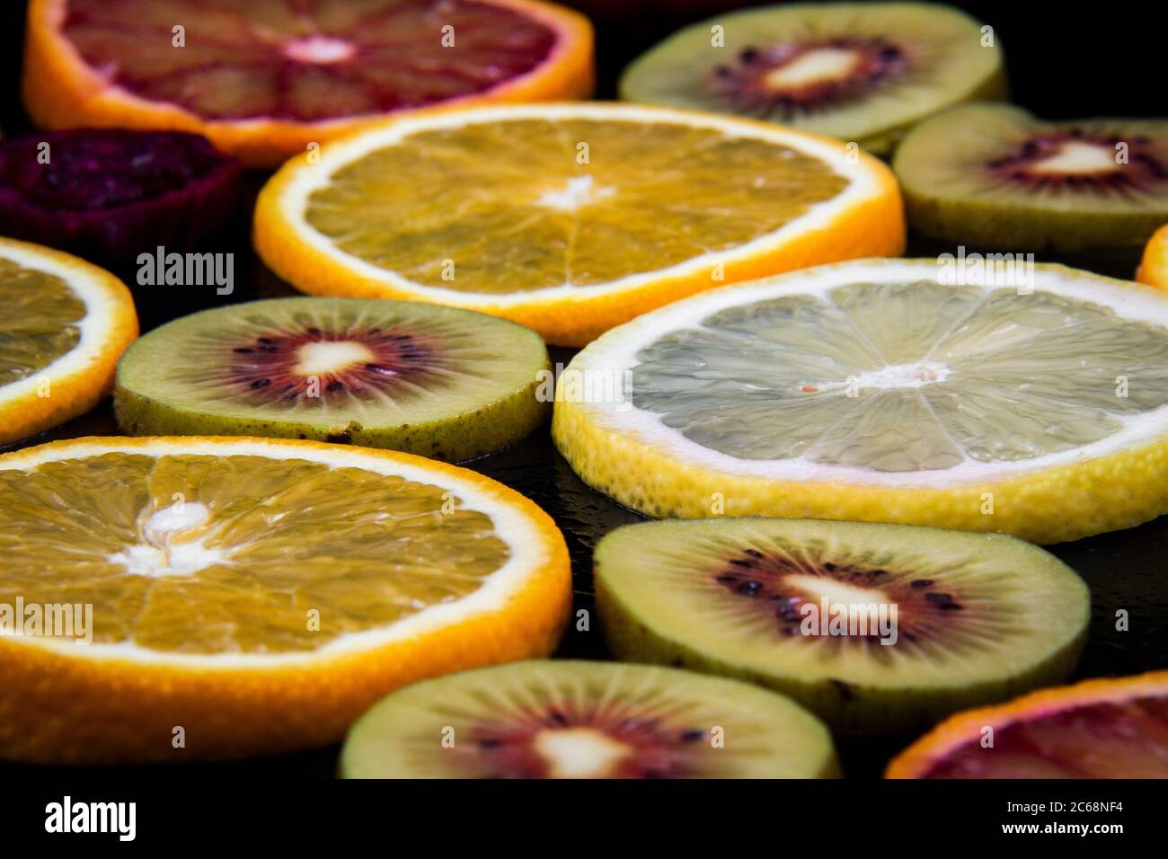Runde Scheiben von roten und gelben Orangen und roten Kiwis auf schwarzem Hintergrund. Stockfoto