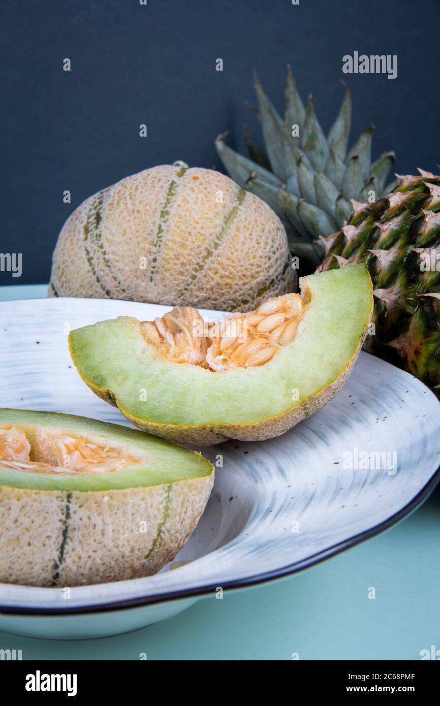 Die Scheiben, die von der Honigmelone in einer Schüssel neben der vollen Melone und der Ananas geschnitten werden. Stockfoto