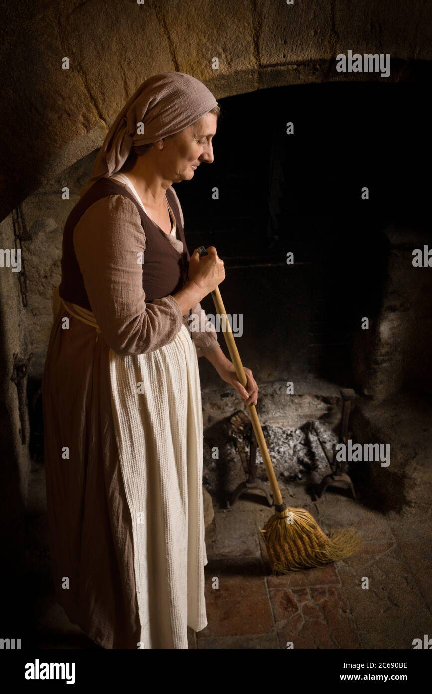 Frau gekleidet in Renaissance Dienstmädchen Kostüm mit ihren Besen den Kamin in der Küche einer Eigenschaft freigegeben Authentische mittelalterliche Burg in Fr zu reinigen Stockfoto