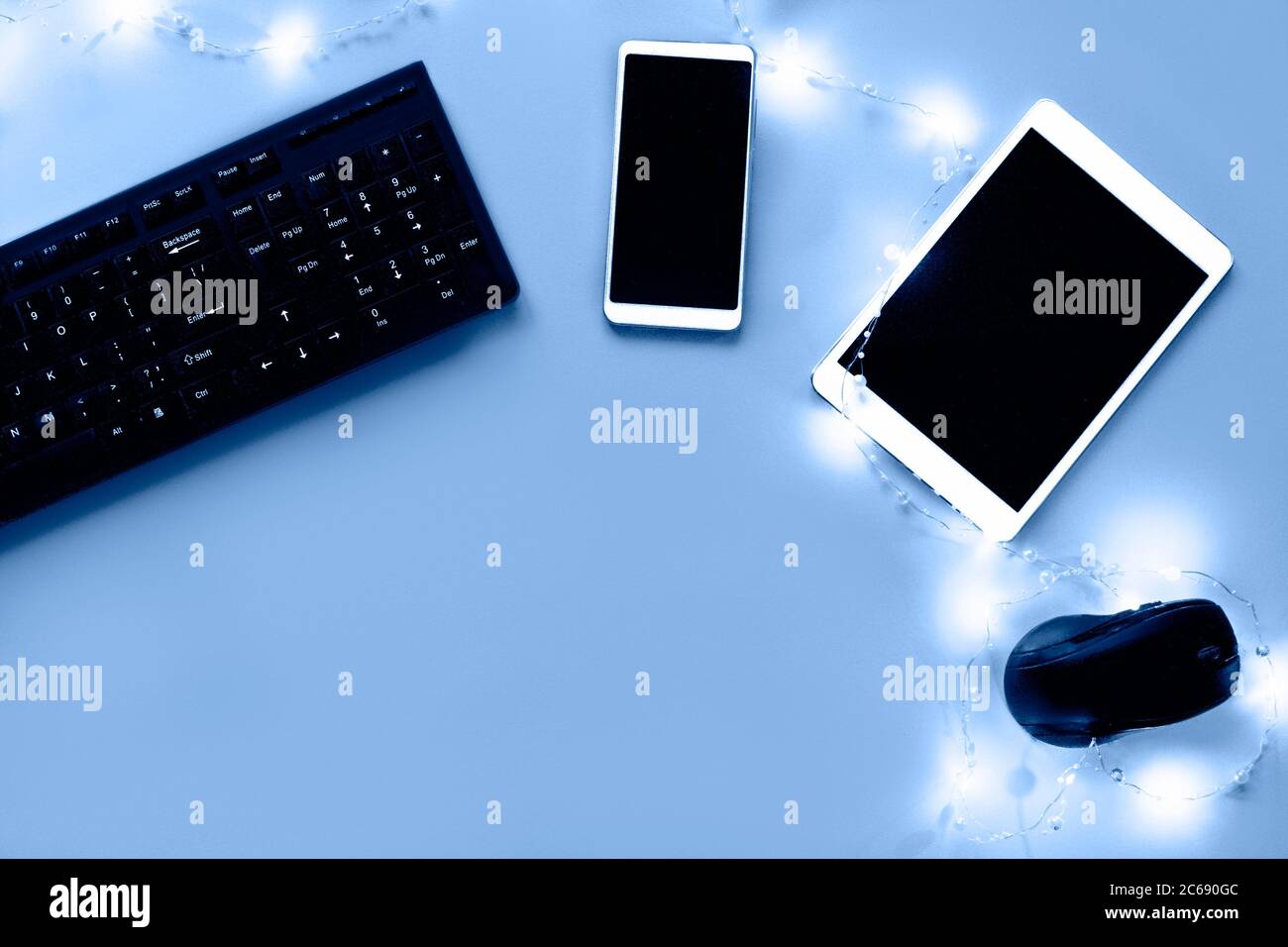 Workstation flach lag auf blauem Hintergrund mit Girlande. Tastatur, Tablet, Telefon, Computer-Maus Zusammensetzung. Speicherplatz kopieren. Stockfoto