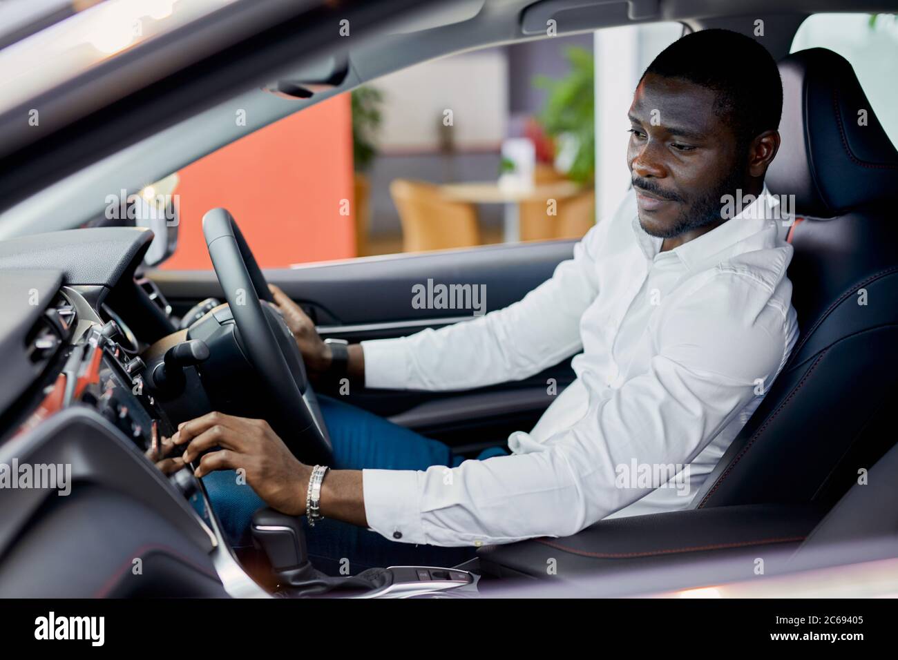 afro Mann sitzt innerhalb des neuen Automobils in Händler, untersucht es, bevor sie Kauf. Auto, Auto-Konzept Stockfoto