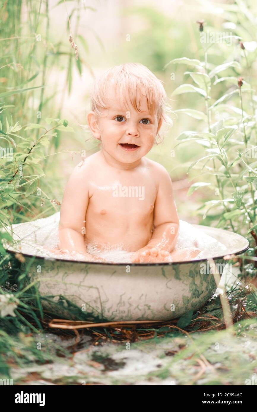 Sonniger Sommertag.EIN charmanter kleiner Junge badete in einem Babybad auf einem grünen Rasen.Er spritzte und lachte. Stockfoto