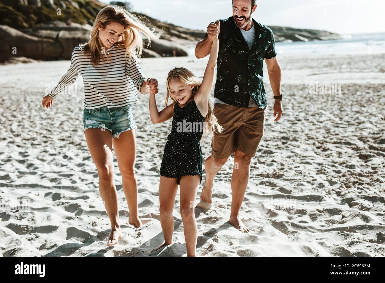 Mädchen spielt mit ihren Eltern am Strand. Familie von drei spielen am Strand an einem Sommerwochenende. Stockfoto
