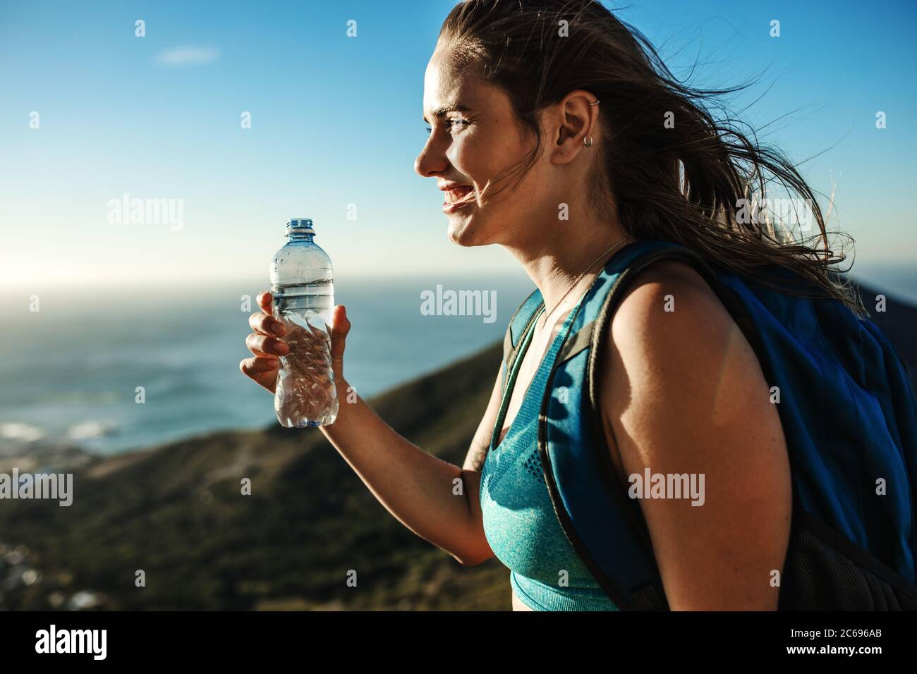 Frau auf der Klippe und Trinkwasser. Bergsteigerin mit einer Wasserflasche in der Hand und Blick auf die schöne Aussicht. Stockfoto