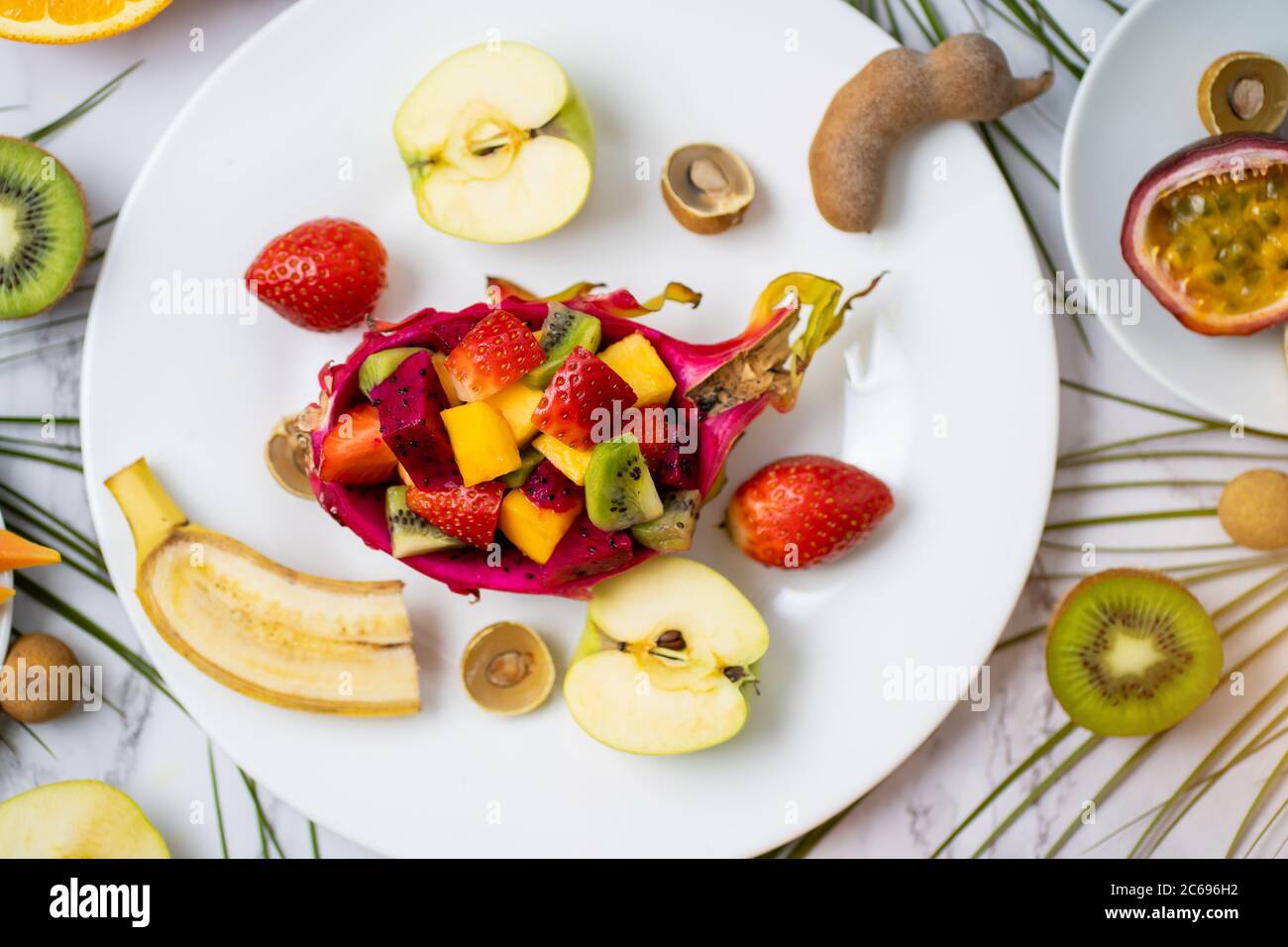 Ein Set exotischer reifer, saftiger, saisonaler tropischer Früchte verteilt sich auf Platte und Tisch. Draufsicht auf geschnittene Früchte und tropische Blätter. Flat Lay Summer com Stockfoto