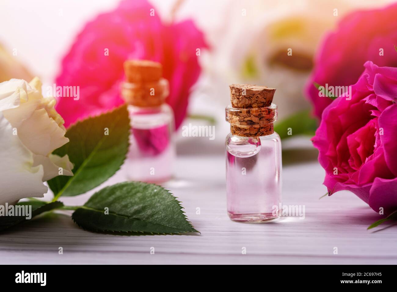 Parfümiertes Rosenwasser oder ätherisches Öl in Glasflaschen mit Blumen auf Holztisch Stockfoto