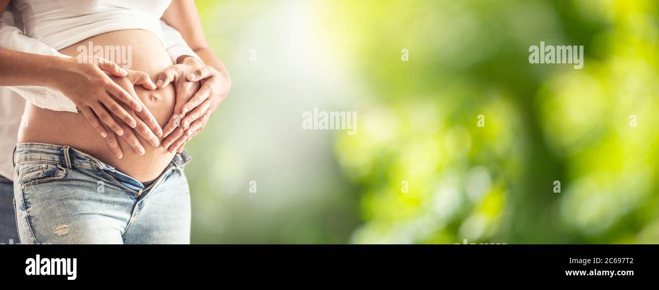 Schwangere Frau mit ihrem Mann umarmt ihren Bauch. Die Hände der zukünftigen Eltern in Erwartung des Babys, das den Bauch in der Form eines Herzens umarmt Stockfoto