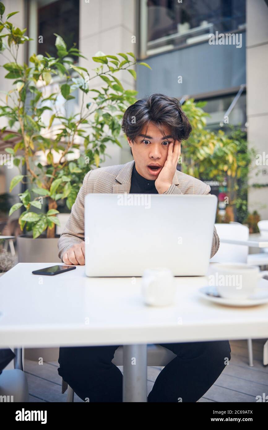 Schockiert junger Mann mit Notebook im Café im Freien Stockfoto