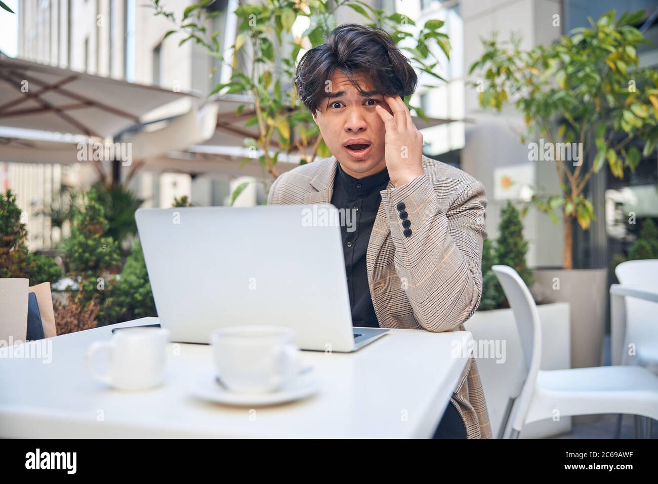 Schockiert junger Mann mit Laptop im Café im Freien Stockfoto