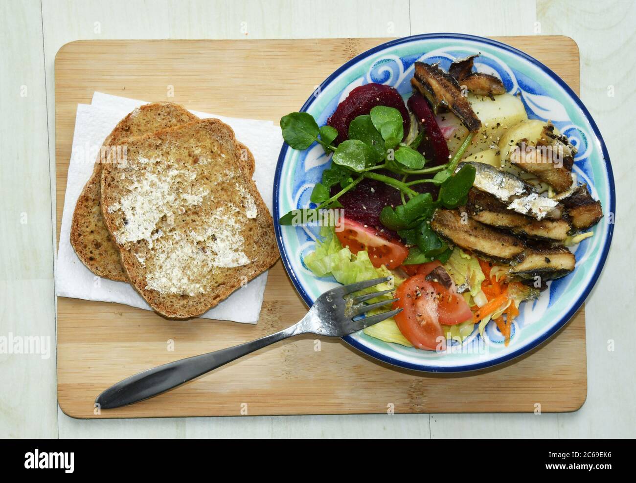 Ein leichtes Mittagessen mit gegrillten Sardinen auf einem Bett mit Krautsalat, Salat, Tomaten, kalten neuen Kartoffeln, Rote Bete und Brunnenkresse mit hausgemachtem Vollkornbrot Stockfoto