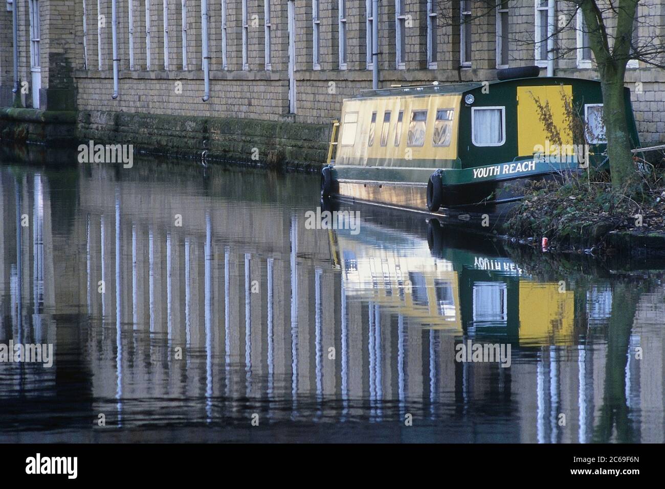 Ein festgetäutes Schmalboot und Salze Mill spiegelt sich im Leeds und Liverpool Canal in Saltaire, West Yorkshire, England, Großbritannien Stockfoto