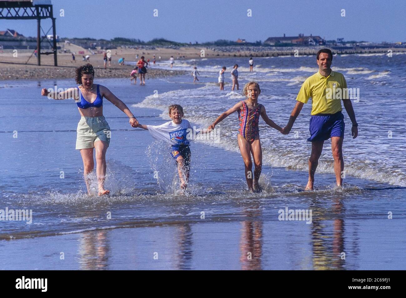 Glückliche junge Familie, die Hände hält und am Meer an einem Sandstrand läuft, Skegness, Lincolnshire, England, Großbritannien Stockfoto