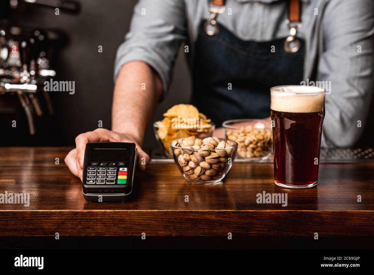 Moderne Bezahlung an der Bar. Der Barkeeper im Vorfeld gibt dem Kunden ein Glas dunkles Bier, Snacks und Terminal Stockfoto