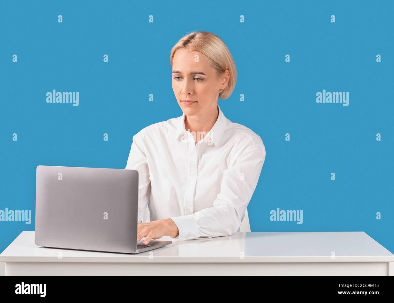 Büroangestellte mit Laptop am Schreibtisch auf blauem Hintergrund Stockfoto