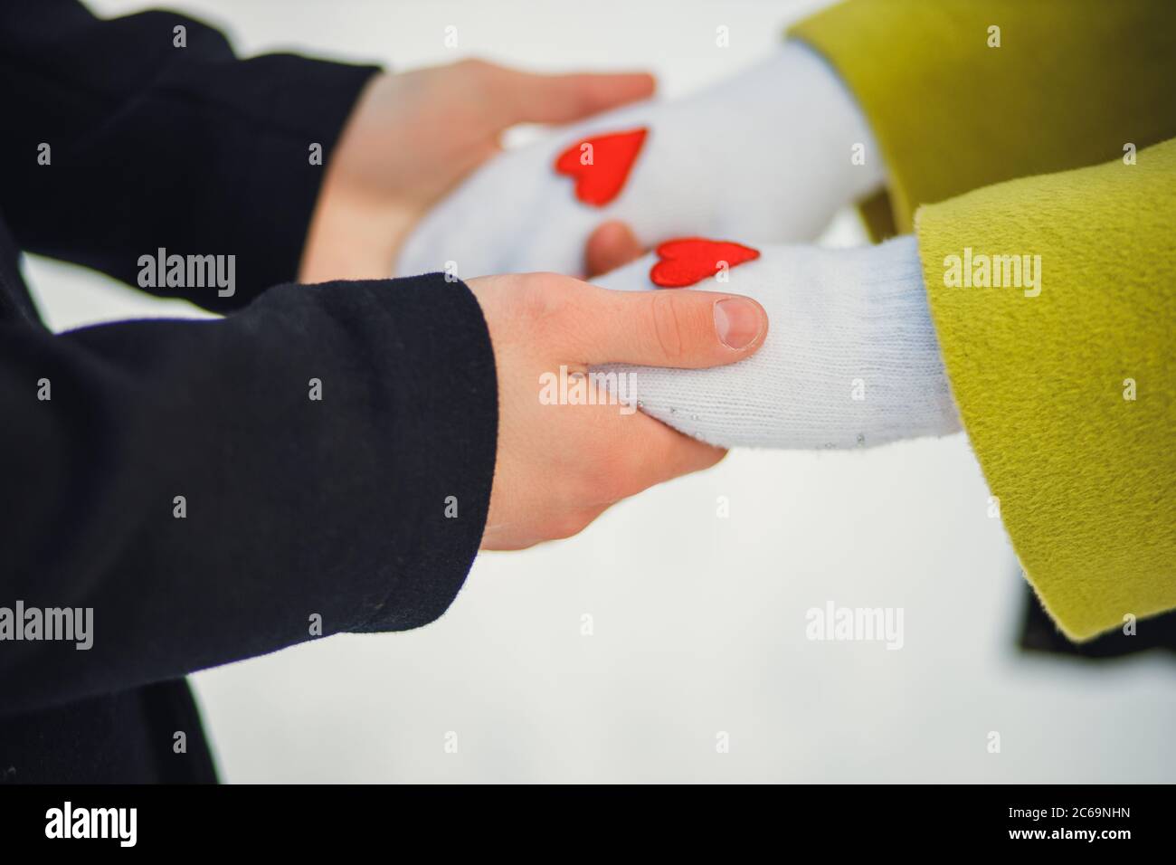 Nahaufnahme Hände von netten Paar in der Winterstraße. Mann halten Hände der Freundin. Kleine rote Herzen auf Handschuhe der Frau. Liebeskonzept. Liebe wärmt Menschen Stockfoto