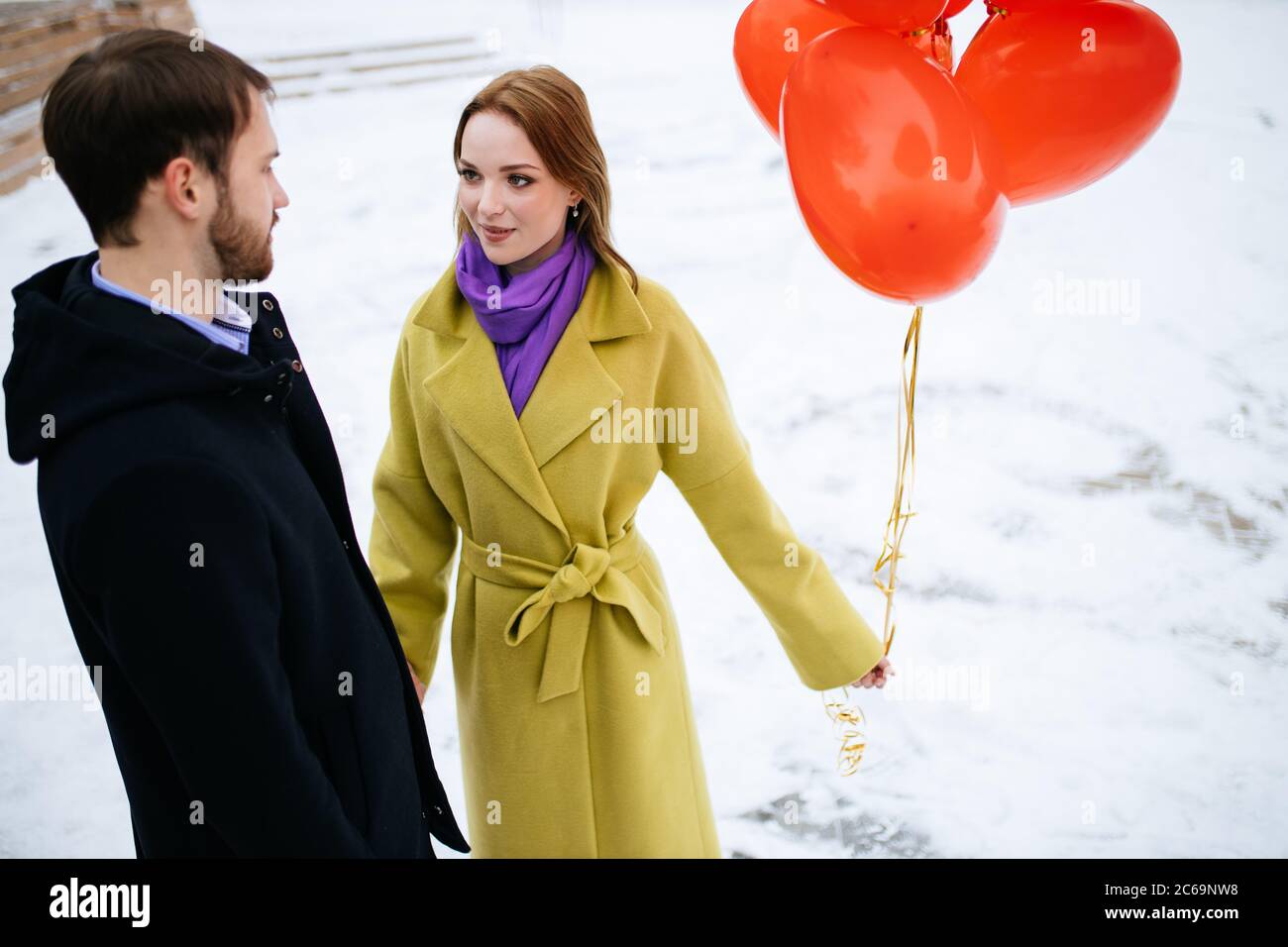 Glücklich kaukasischen Paar verbringen Freizeit zusammen im Freien, Mann und Frau in Mänteln, mit roten Luftballons in den Händen. Liebe, Beziehungen Konzept Stockfoto