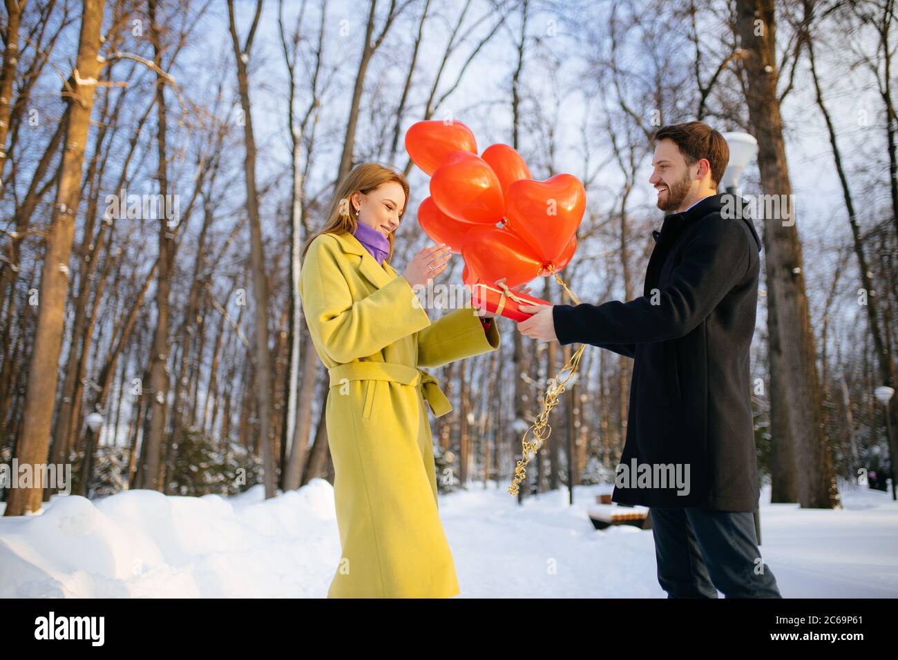 Seitenansicht auf schöne Paar feiert Jubiläum im Freien. Mann geben Geschenk in kleinen roten Box, um Dame im grünen Mantel, sie ist glücklich, verliebt. Winter pa Stockfoto