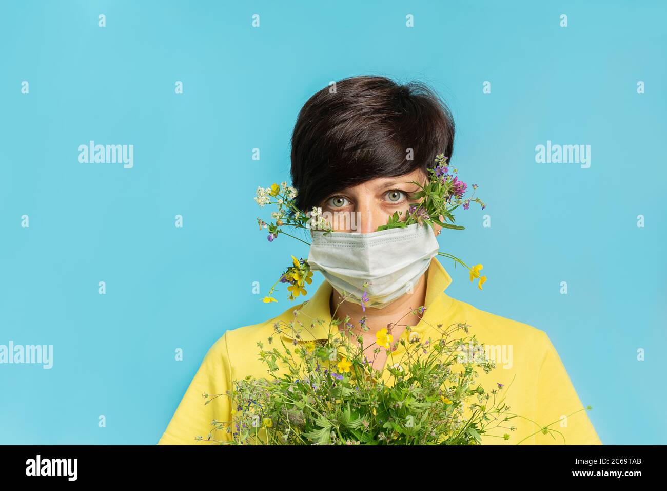 Frau in schützende medizinische Maske hält frische Blumen auf blauem Hintergrund. Das Konzept der Gesundheit und Allergieprävention Stockfoto