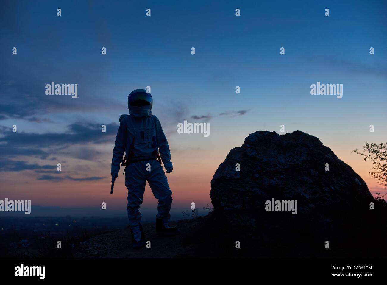 Silhouette von tapferen Raum Reisenden auf felsigen Berg mit schönen Sonnenuntergang im Hintergrund stehen. Kosmonauten tragen weißen Raum Anzug mit Helm. Konzept der Raumfahrt und Schönheit der Dämmerung. Stockfoto