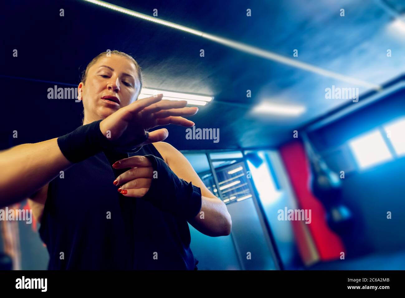 Frau im Fitness-Salon bereitet sich auf ihr Kickboxen-Training vor. Sie trägt Schwarz und bindet eine Art Verband an ihre Hände Stockfoto