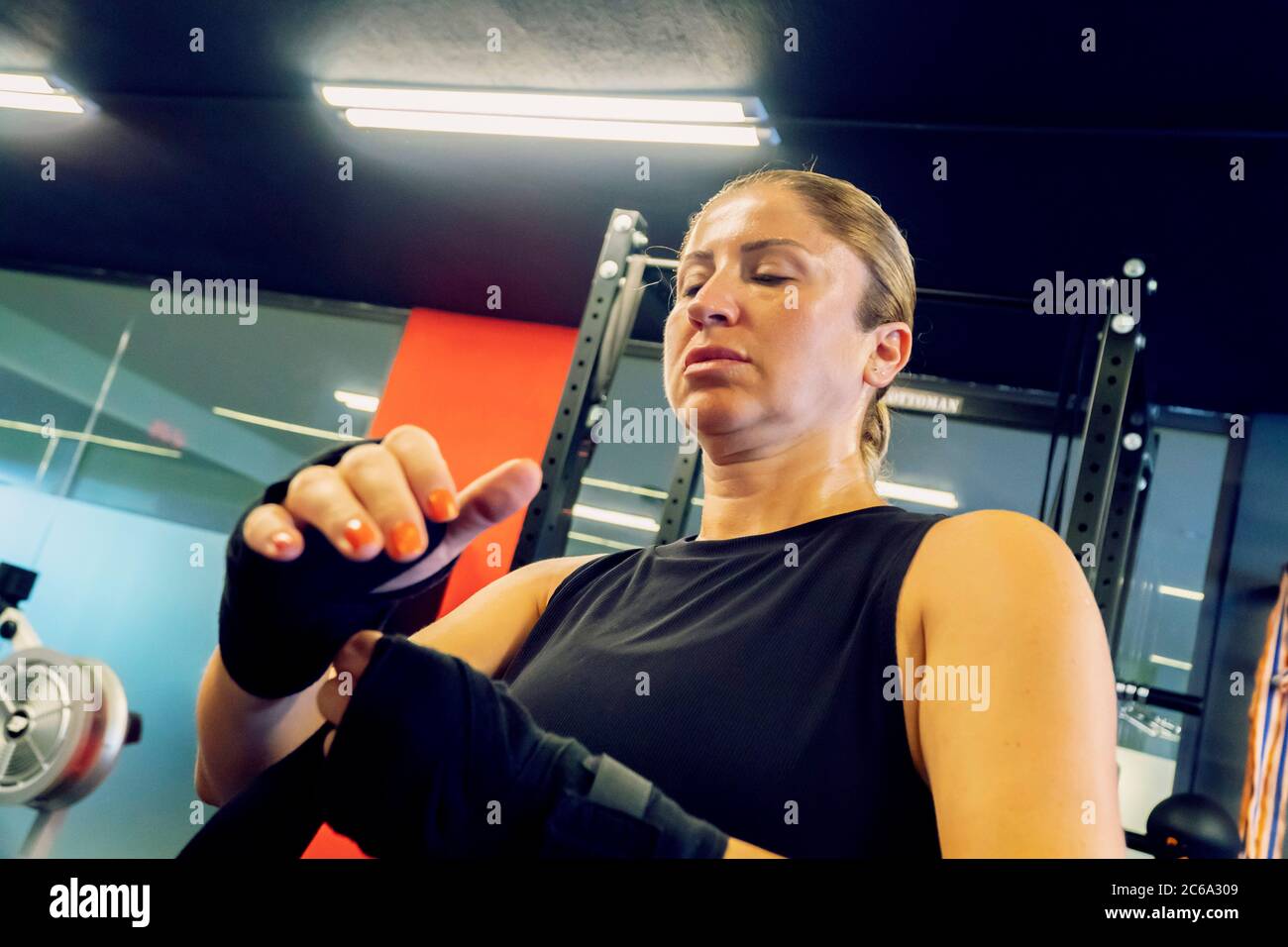Frau im Fitness-Salon bereitet sich auf ihr Kickboxen-Training vor. Sie trägt Schwarz und bindet eine Art Verband an ihre Hände Stockfoto