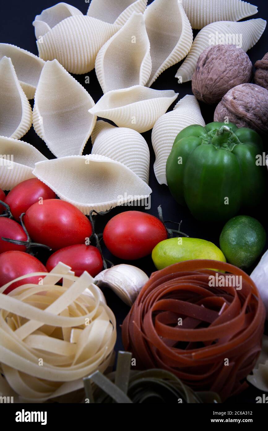 Bunte und bunte Pasta in großer Zahl und in verschiedenen Farben zusammen mit verschiedenen Früchten und Gemüse. Stockfoto
