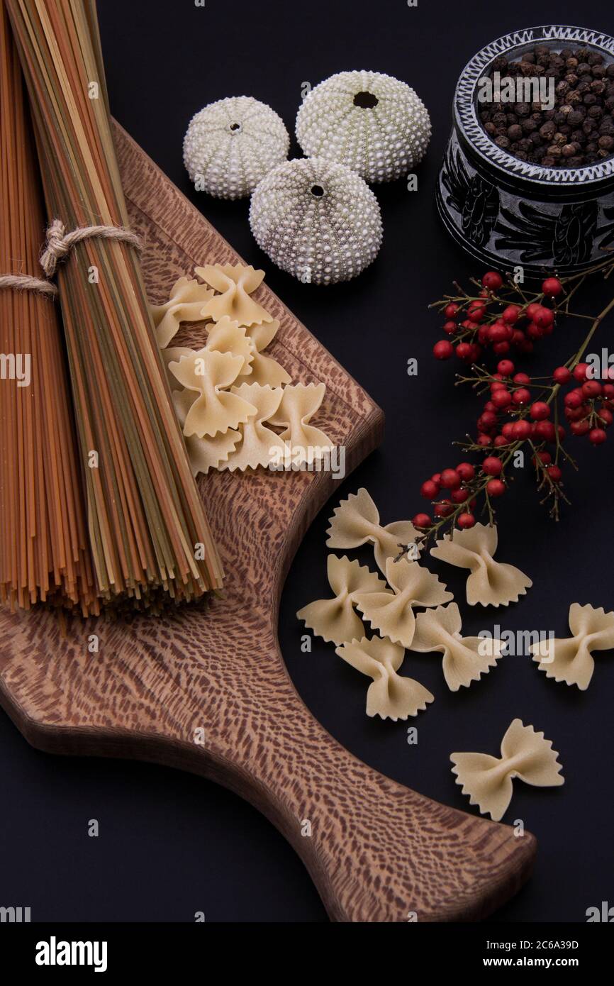 Lange braune Pasta und Pasta mit verschiedenen Formen und Farben mit einer Schüssel Pfeffer. Stockfoto