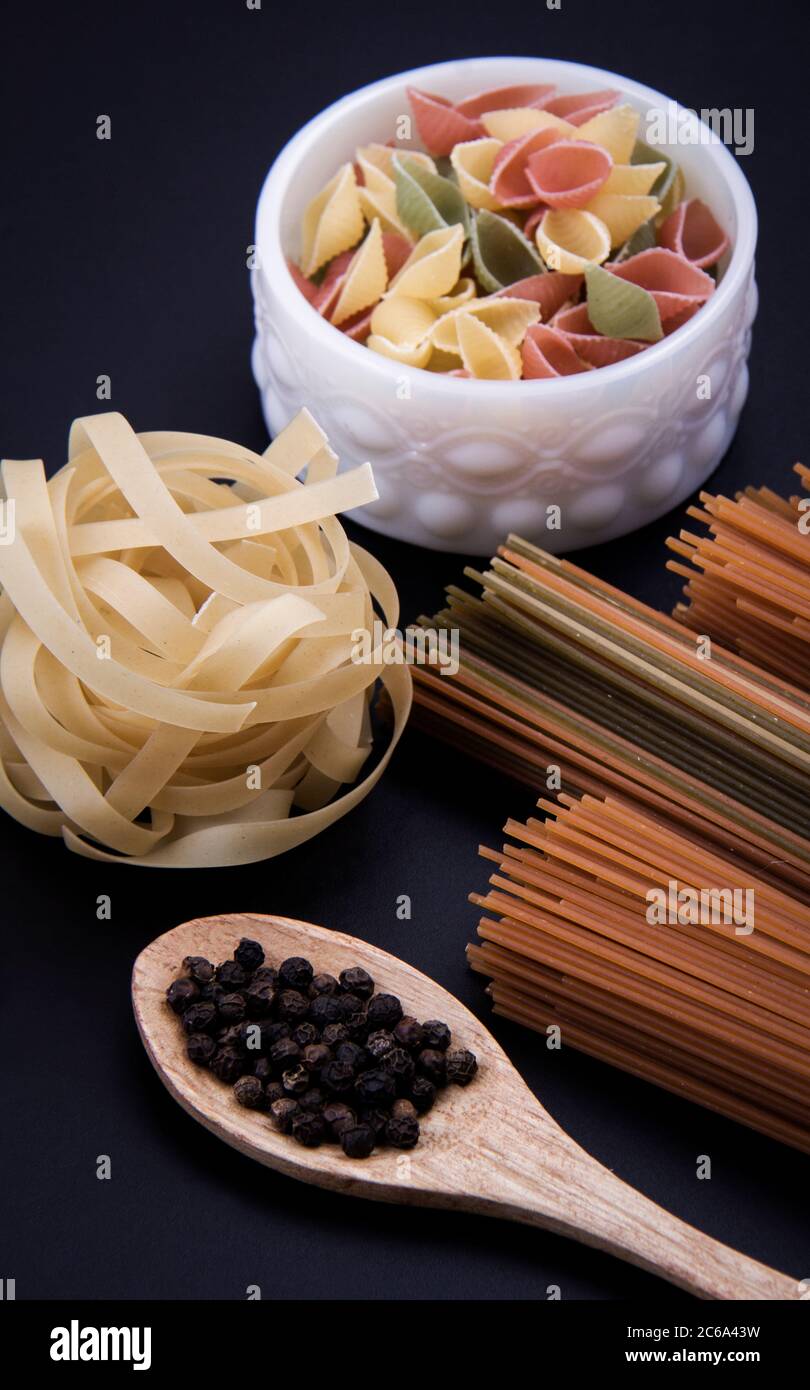 Lange braune Pasta und geformte Pasta neben einer Schüssel mit schwarzem Pfeffer. Stockfoto