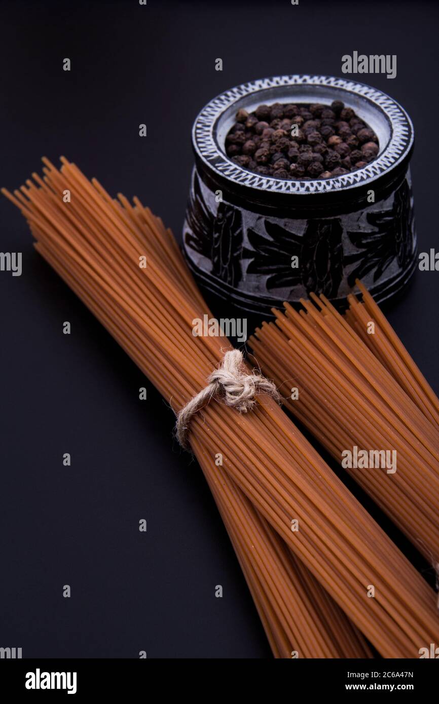 Lange braune Pasta in verschiedenen Größen mit einer Schüssel schwarzen Pfeffer. Stockfoto