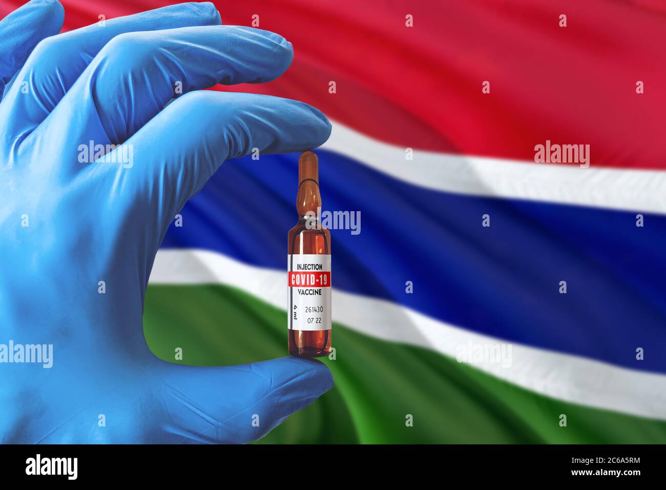 Gambia Flagge mit Coronavirus Covid-19 Konzept. Arzt mit blauen Schutzhandschuhen mit einer Impfstoffflasche. Epidemic Virus, Cov-19, Corona vir Stockfoto