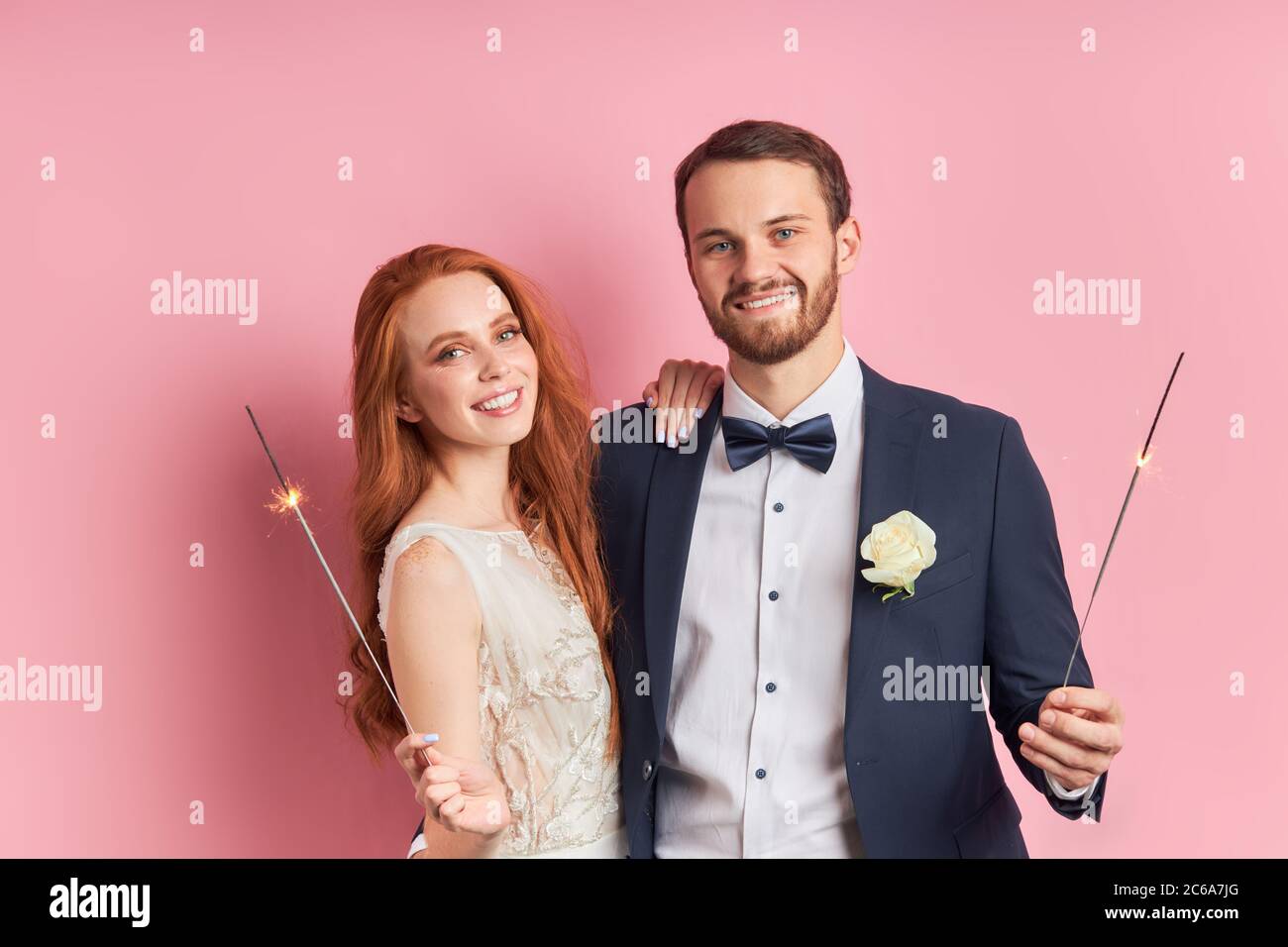 Kaukasisches Paar zelebriert ihre Ehe nach einem Jahr. Rothaarige Frau in weißem Kleid lächelnd, halten Wunderkerzen in den Händen. Mann in Smoking in der Liebe mit w Stockfoto