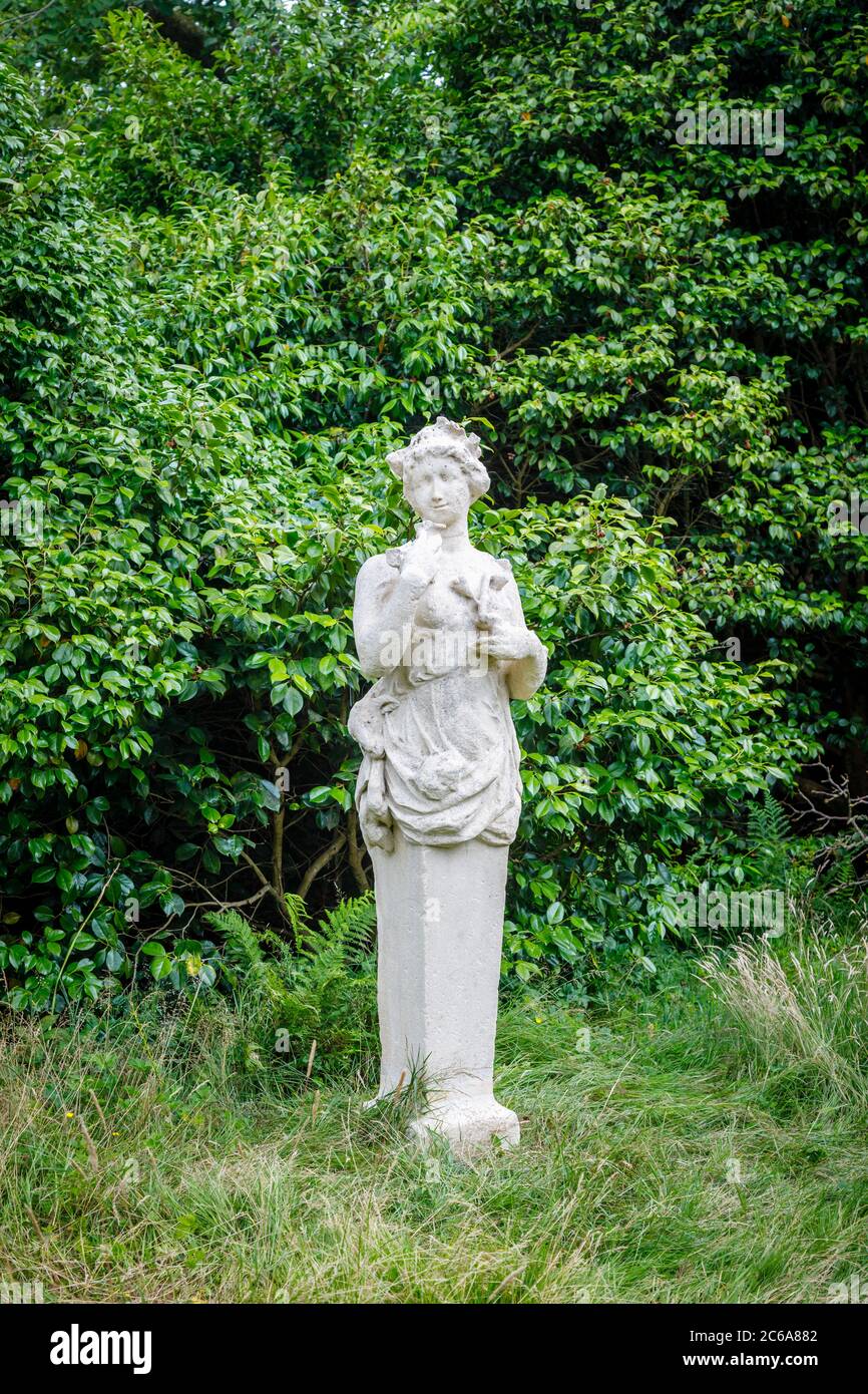 Klassische leicht erodierte Vintage-Steinstatue einer weiblichen Nymphe oder Dryade, die in einem Garten im Südosten Englands vor einem grünen Heckenhintergrund steht Stockfoto