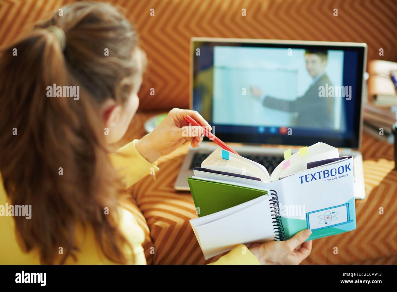 Von hinten gesehen Frau mit Videokonferenz mit einem Lehrer auf einem Laptop zu Hause an sonnigen Tag. Stockfoto