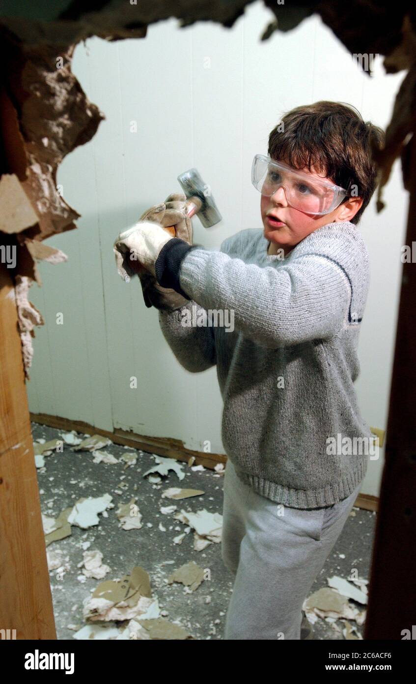 Austin Texas, USA, 2003: Ein achtjähriger Junge mit Schutzbrille verwendet einen Vorschlaghammer, um beim Umbau des Büros Trockenbauwände zu zerschlagen. Modell Freigegeben. ©Bob Daemmrich Stockfoto