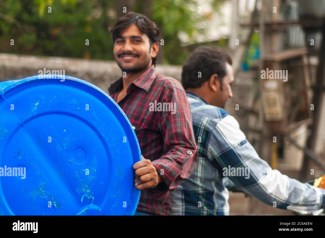 Ein indischer Mann, der mit einer Trommel rückwärts auf dem Sozius reitet. Dies ist ein Beispiel für 'jugaad' oder eine nicht-konventionelle Lösung, um eine Trommel auf einem Fahrrad zu tragen. Stockfoto