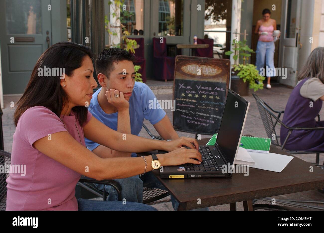 Austin, Texas, USA, August 2003: Hispanische Fachfrau (28) und hispanische männliche Freundin (21) nutzen Laptop und kabellose Internetverbindung in einem Café im Freien in der Sommerhitze. HERR ©Bob Daemmrich Stockfoto