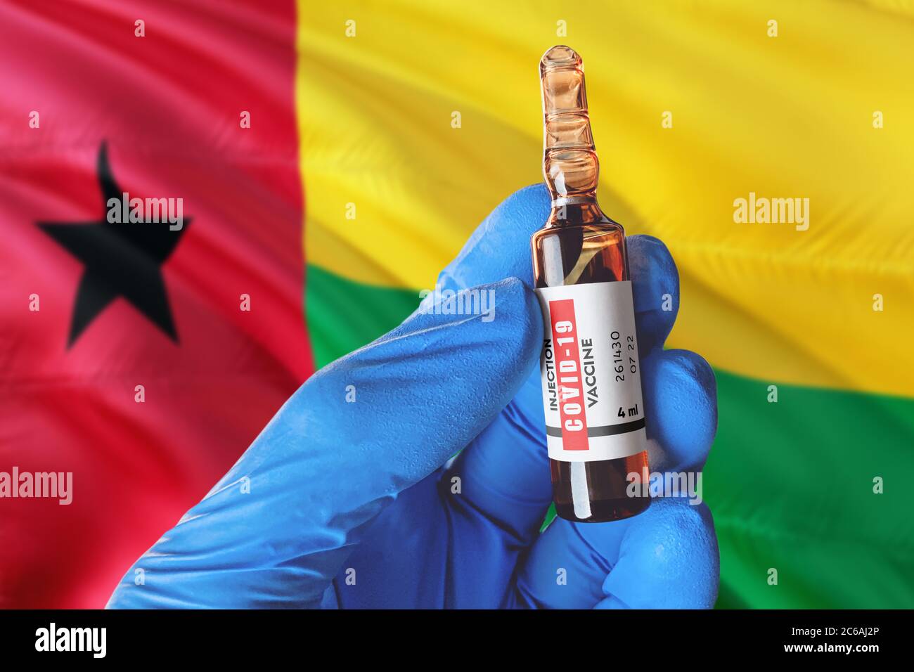Guinea Bissau Flagge mit Coronavirus Covid-19 Konzept. Arzt mit blauen Schutzhandschuhen hält eine Impfstoffflasche. Coronavirus covid 19 Impfstoff Stockfoto