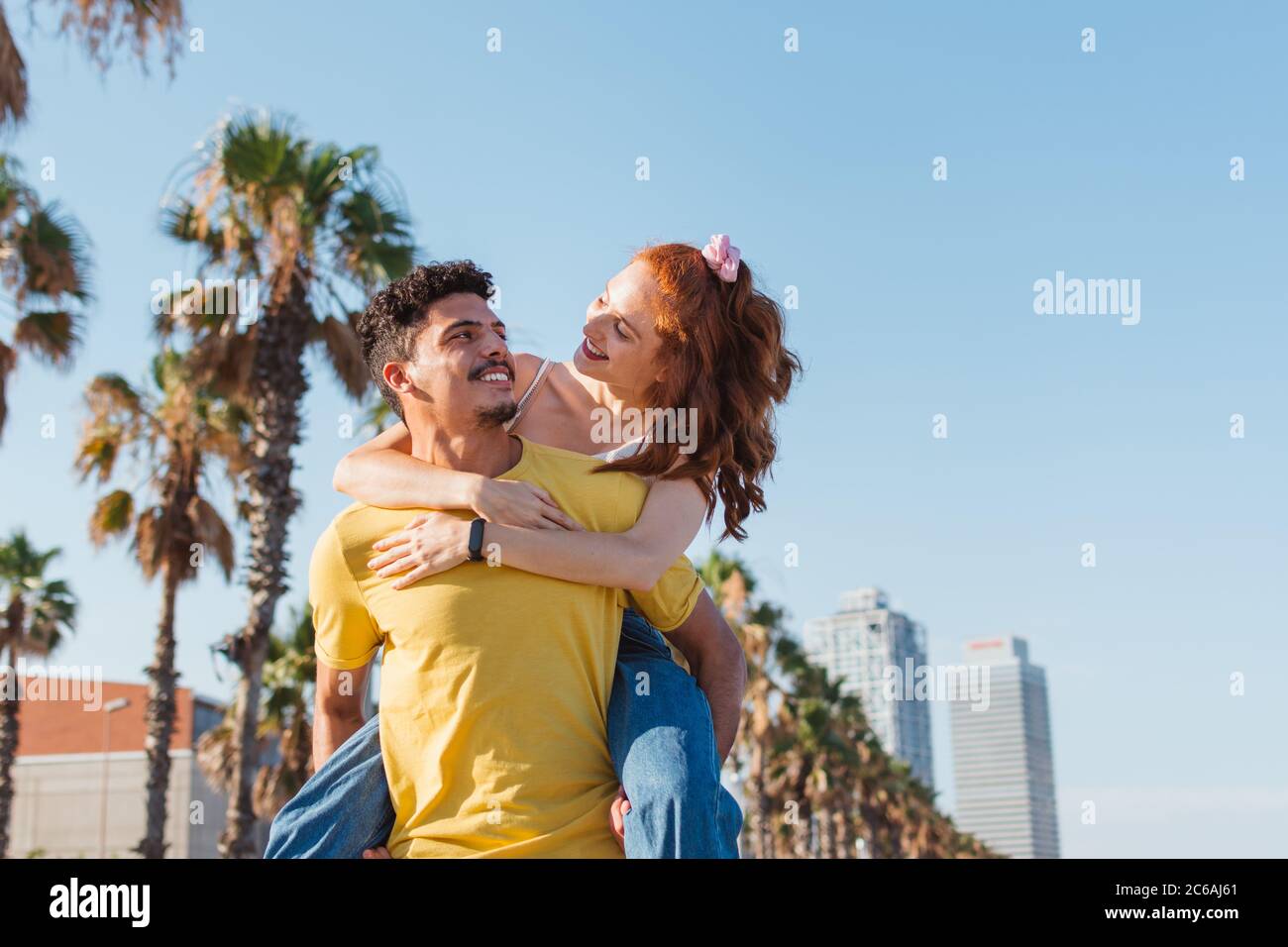 Der junge Mann trägt seine Freundin auf dem Rücken und lächelt Stockfoto