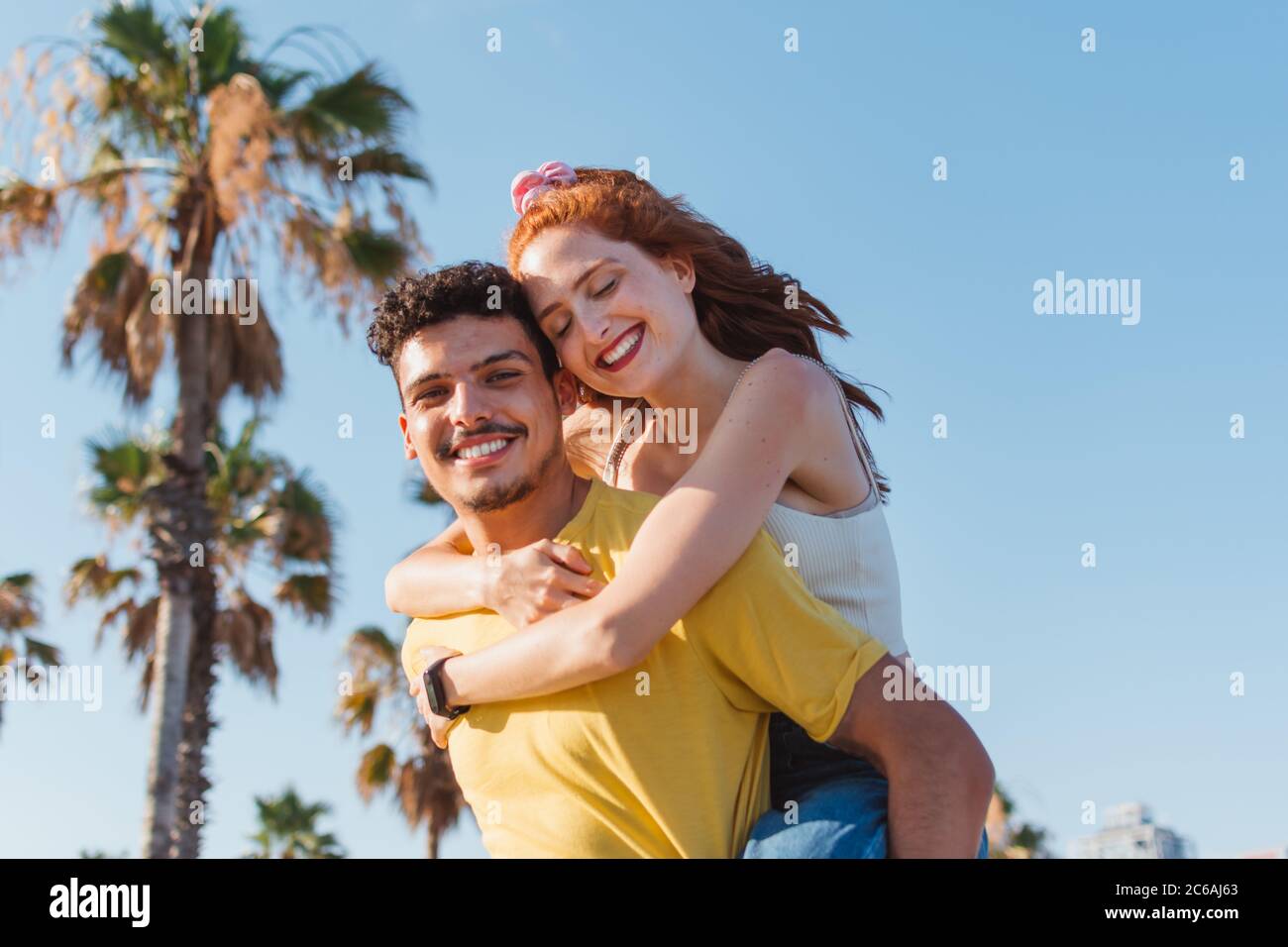 Der junge Mann trägt seine Freundin auf dem Rücken und lächelt Stockfoto