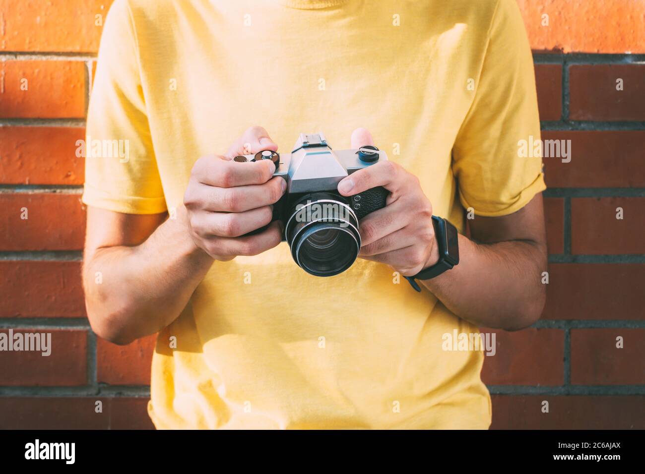 Der junge Mann in Gelb hält in den Händen eine analoge Kamera Stockfoto