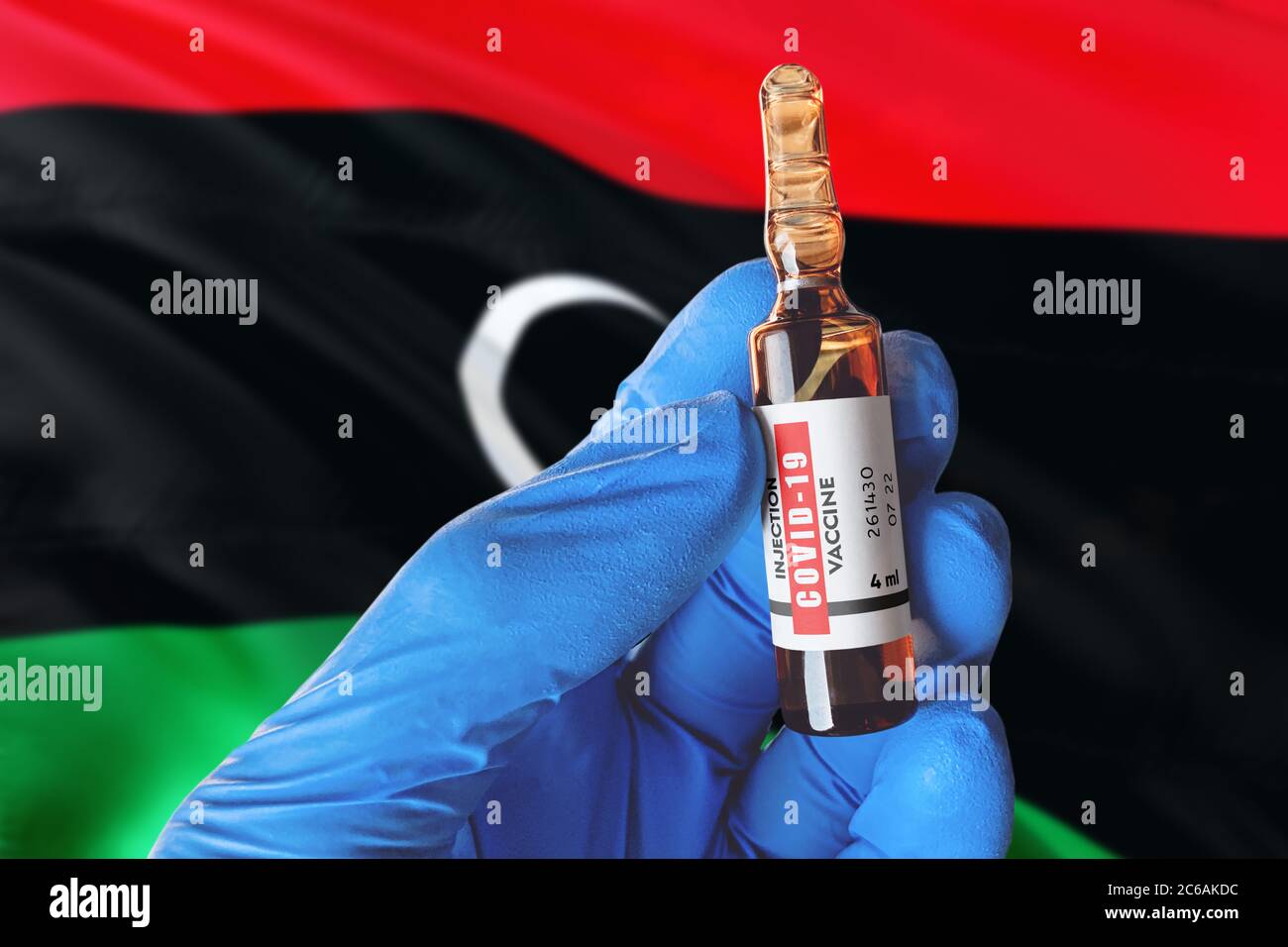 Libyenflagge mit Coronavirus Covid-19 Konzept. Arzt mit blauen Schutz medizinische Handschuhe hält eine Impfstoffflasche. Coronavirus covid 19 Impfstoffforschung Stockfoto