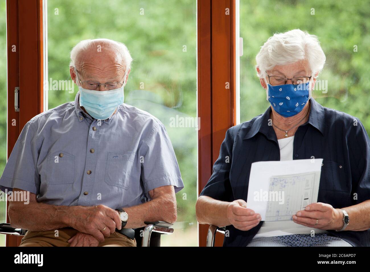 Seniorenpaar sitzt mit Gesichtsmasken in einem hellen Wartezimmer eines Krankenhauses oder eines Büros Stockfoto