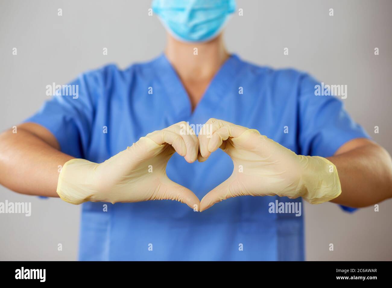 Arzt in einer Gesichtsmaske und Handschuhe bilden ein Herz vor blauem Hemd, Stockfoto