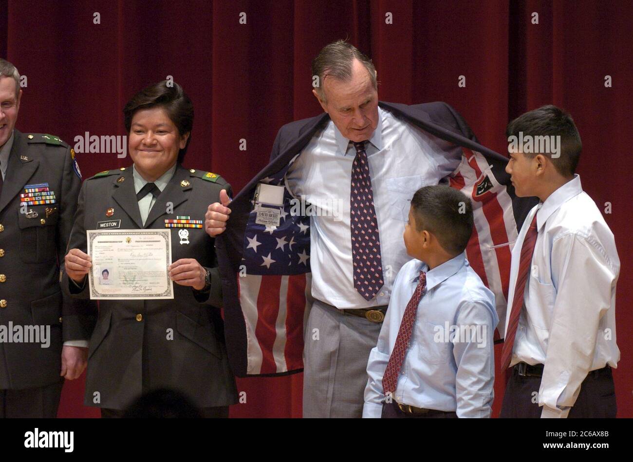 College Station, Texas, USA, 11. März 2005: Früher USA Präsident George HW Bush zeigt Edward (9) und Alex (12) Weston seine Sportjacke mit einer amerikanischen Flagge, während ihre Mutter, Sergeant Rosa Weston, ihr neues US-Staatsbürgerschaftszertifikat bei Zeremonien an der Texas A&M University vorlegt. ©Bob Daemmrich Stockfoto