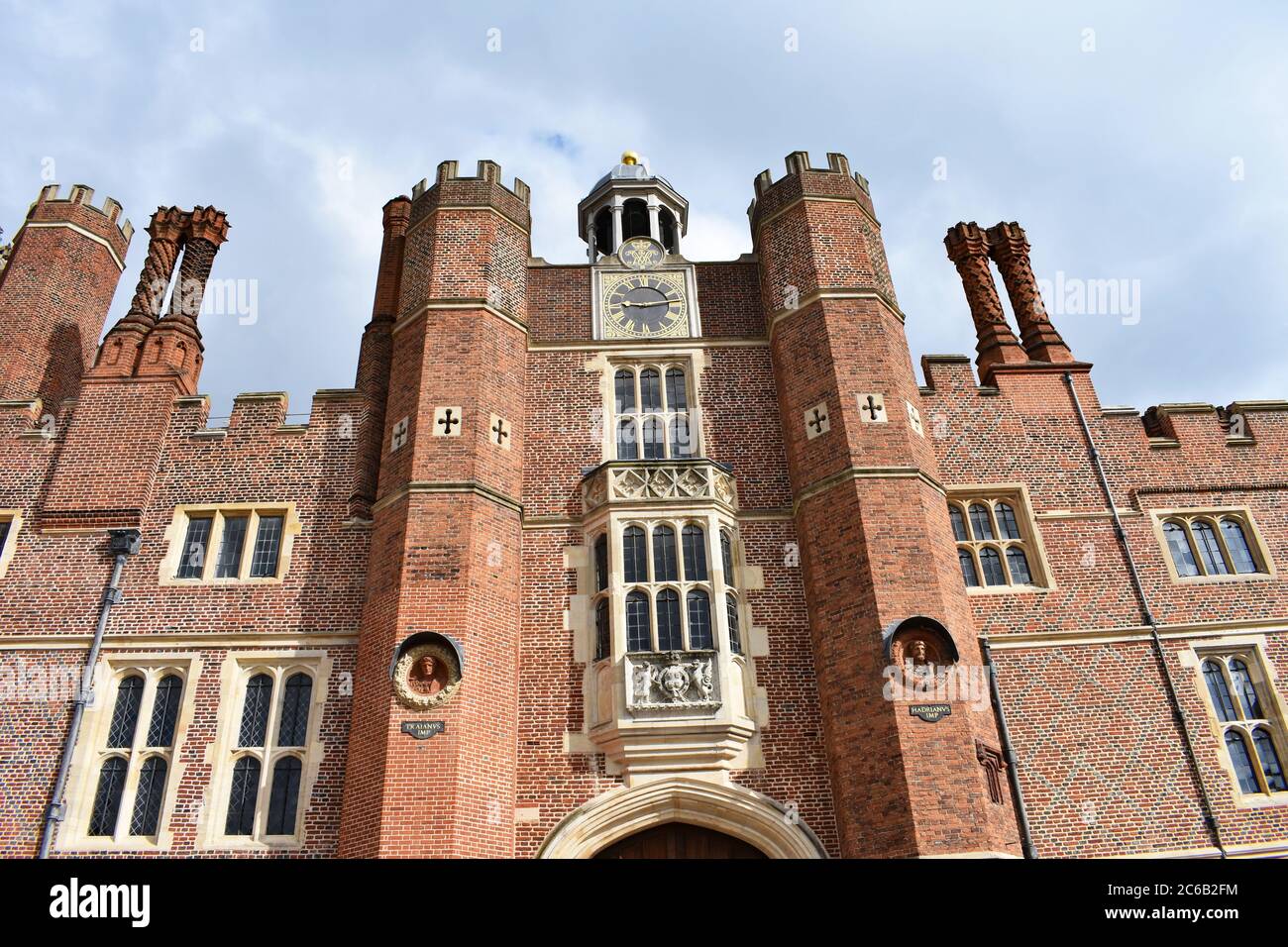 Ein Blick auf das Tudor-Mauerwerk im Hampton Court Palace. Der Uhrenturm im Basisgericht. Vier Kamine erheben sich aus dem Gebäude. Bewölktes Wetter. Stockfoto