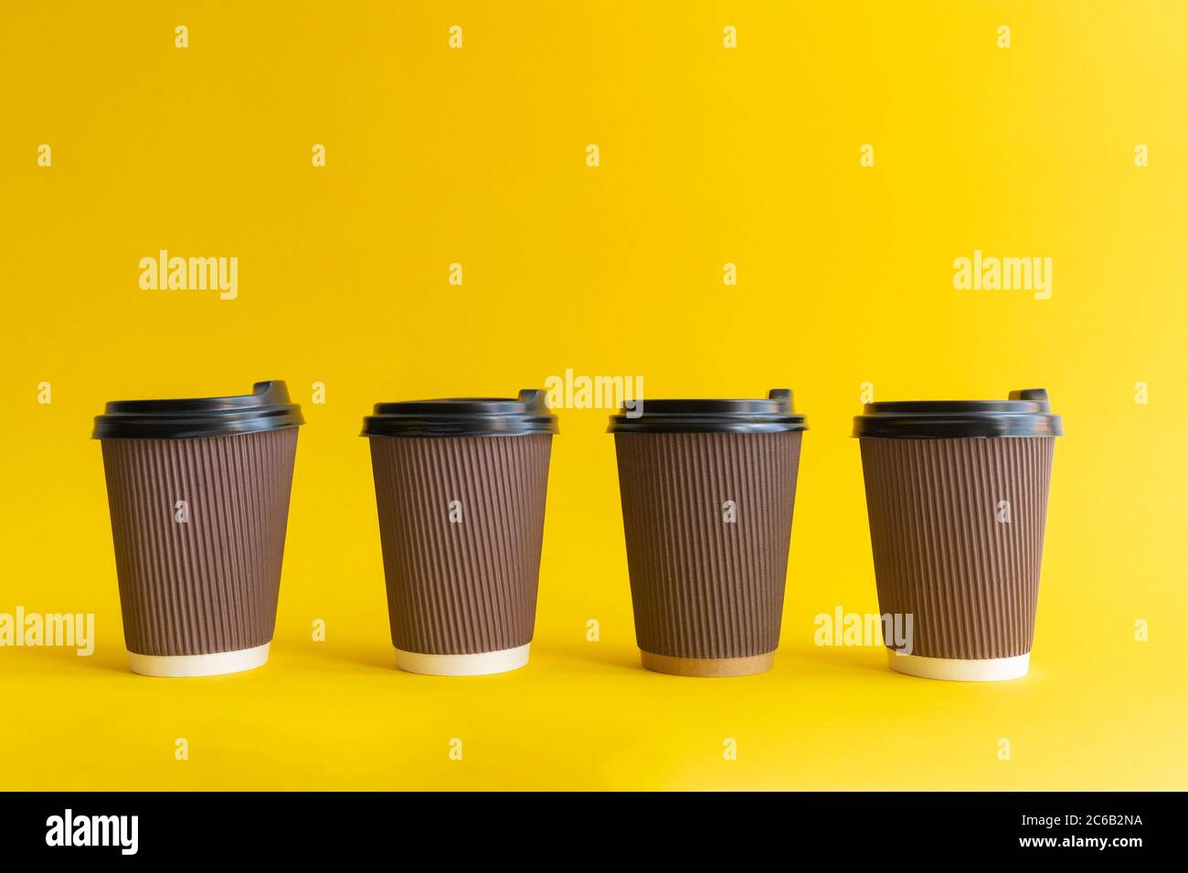 Vier braune togo Kaffeetassen mit schwarzen Bezügen auf gelbem Hintergrund, Stockfoto