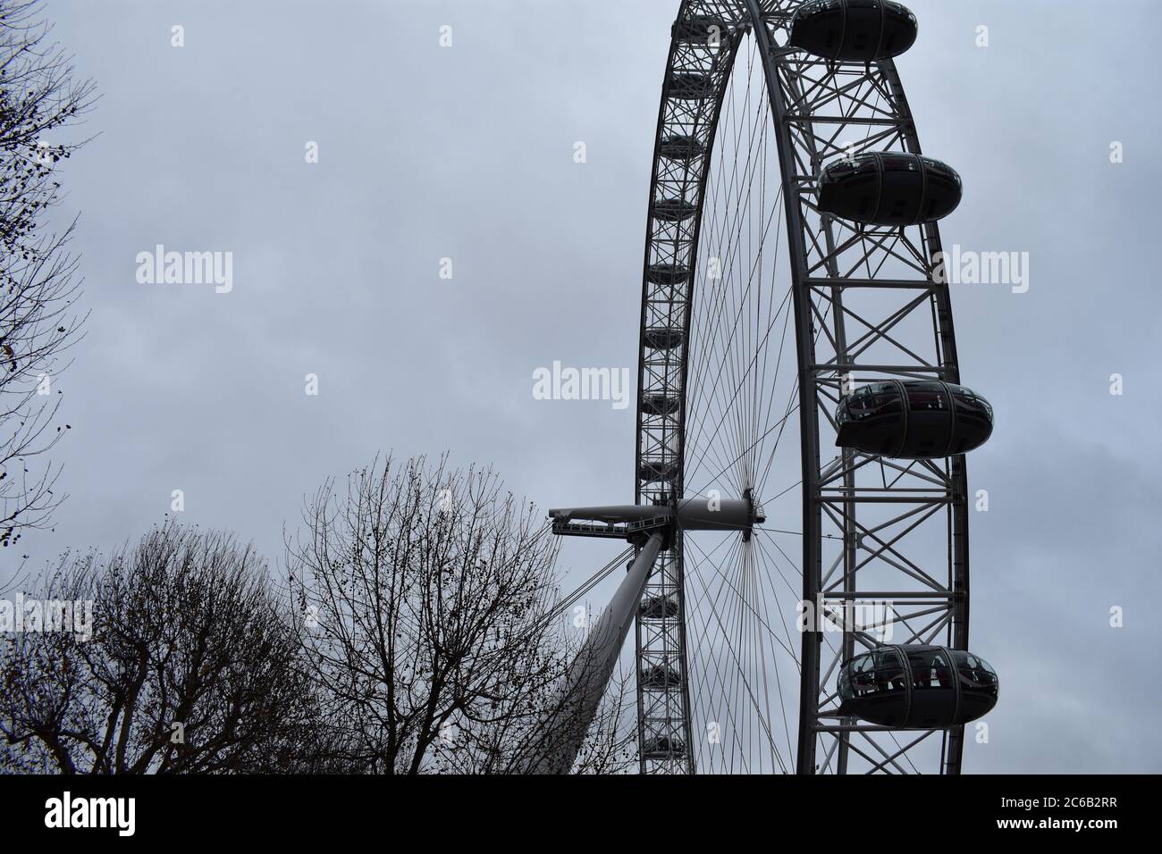 Das London Eye. Ein riesiges Beobachtungsrad auf dem Südufer. Ein Teil des Rades wird an einem wolkigen Wintertag mit Bäumen um den Rand des Bildes gezeigt. Stockfoto
